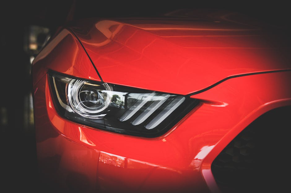 Detailed view of a red Ford Mustang's headlight showcasing sleek automotive design.